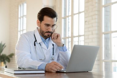 Bilgisayarda çalışan ciddi genç erkek doktorlara odaklanmış..