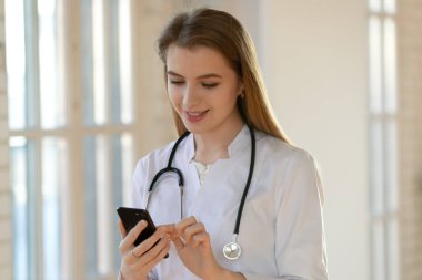 Gülümseyen genç pratisyen doktor akıllı telefon kullanıyor..