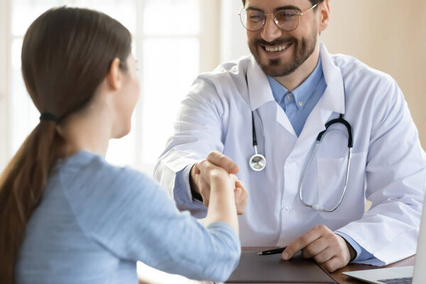 Smiling young handsome male doctor shaking hands with female patient.