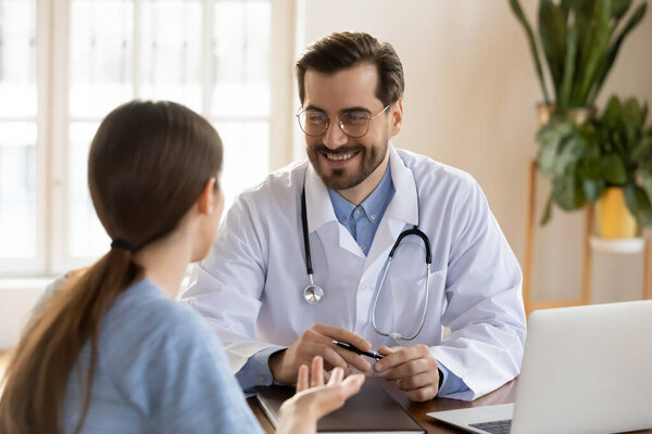 Smiling young male general practitioner in uniform listening to woman.