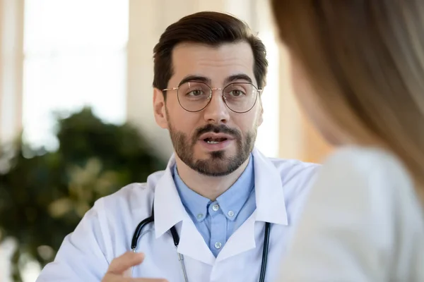Fokuserad ung manlig läkare som förklarar hälso- och sjukvårdsbehandling för patienten. — Stockfoto
