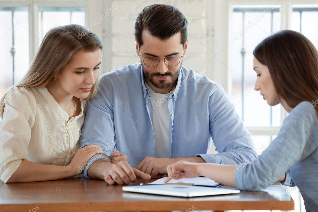 Focused young married couple discussing agreement with skilled broker.
