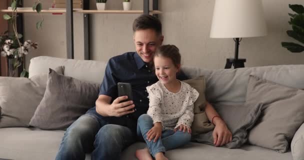 Χαμογελώντας νεαρός πατέρας δείχνει αστεία εφαρμογές για κινητά στην κόρη. — Αρχείο Βίντεο