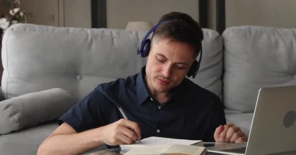 Konzentrierter junger gutaussehender Mann mit Kopfhörer, der distanziert studiert. — Stockvideo