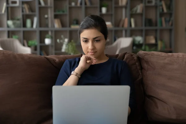 Pensive young Indian woman work on computer thinking