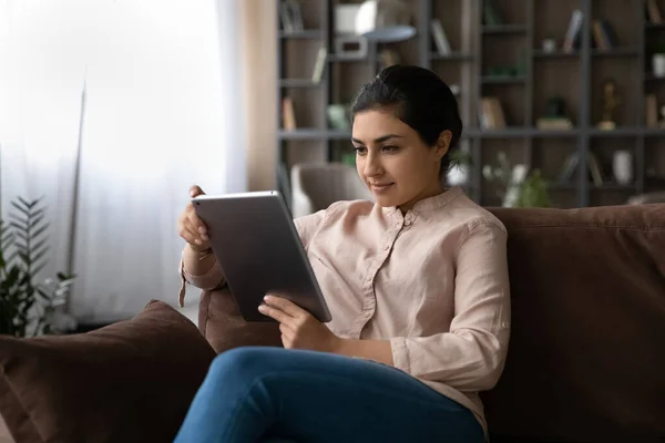 Young Indian woman relax on sofa using tablet