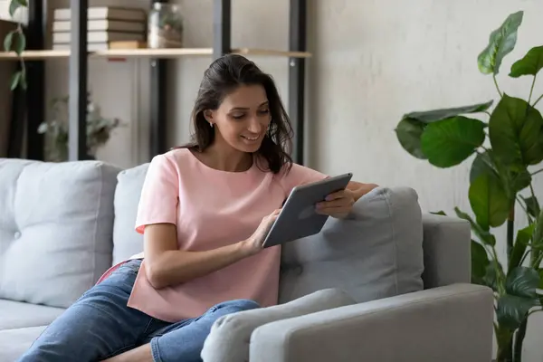 Usmívající se indická žena relaxující na pohovce doma pomocí tabletu — Stock fotografie