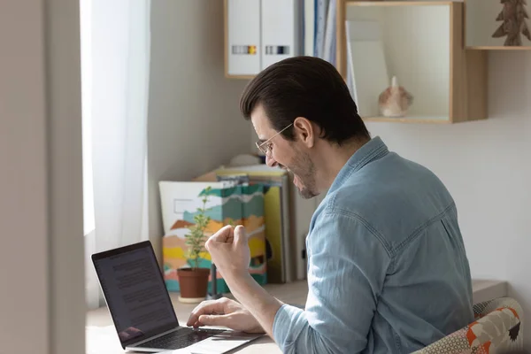 Excited millennial man triumph with good news on laptop