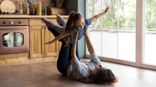 Fürsorgliche Mutter hält kleine Tochter auf dem Boden liegend und täuscht Fliegen vor — Stockfoto