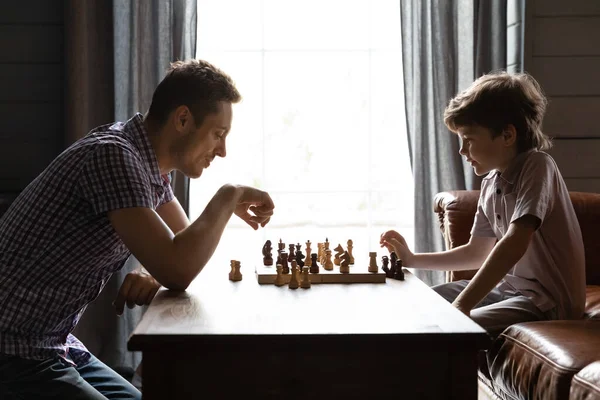 Vista lateral pai e filho pequeno jogando xadrez em casa — Fotografia de Stock
