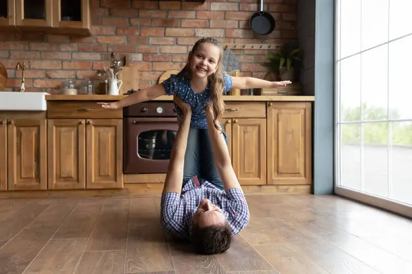 Padre premuroso che tiene la figlioletta che finge di volare, sdraiato sul pavimento — Foto Stock