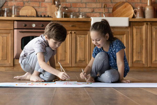 Двое маленьких детей рисуют красочную акварель, сидя на полу
