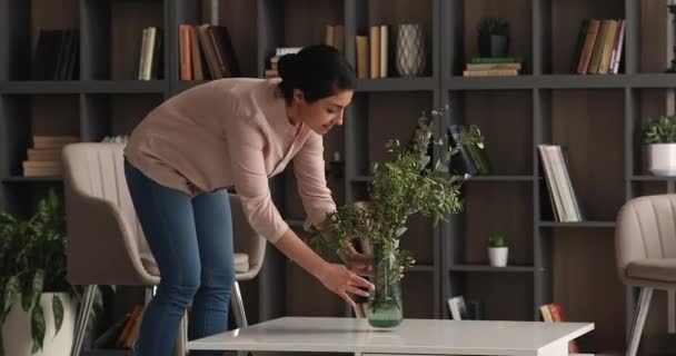 Sorrindo arrumado jovem indiana colocando vaso com flores na mesa. — Vídeo de Stock