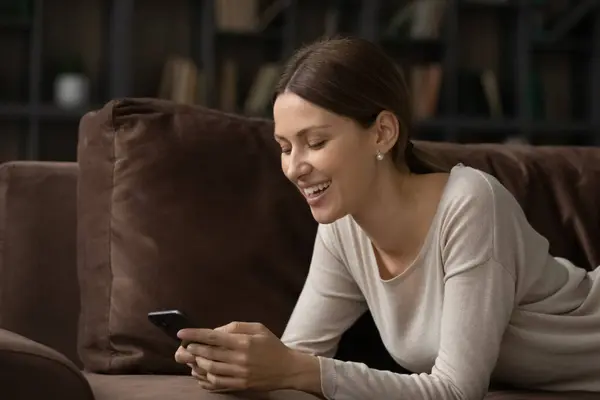 Mujer feliz relajarse en el sofá mensajes de texto en línea en la celda — Foto de Stock