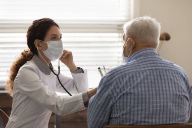 Yüz maskesi takan kadın doktor olgun erkek ciğerlerini kontrol ediyor.