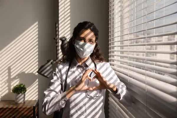 Kalp hareketi gösteren tıbbi maske takan profesyonel bir kadın doktor. — Stok fotoğraf