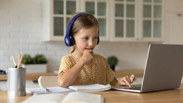 Geïnteresseerd schoolmeisje in headset kijken onderwijs video les van thuis — Stockfoto