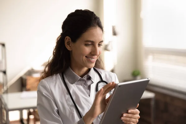 Close up smiling female doctor using tablet, standing in office