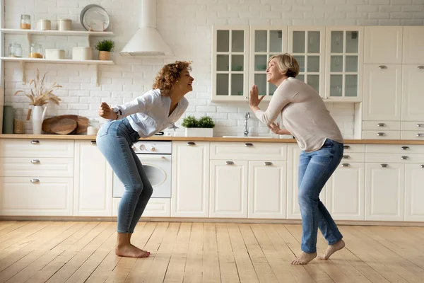 Hija adulta y madre bailando en la cocina moderna celebran la renovación —  Fotos de Stock