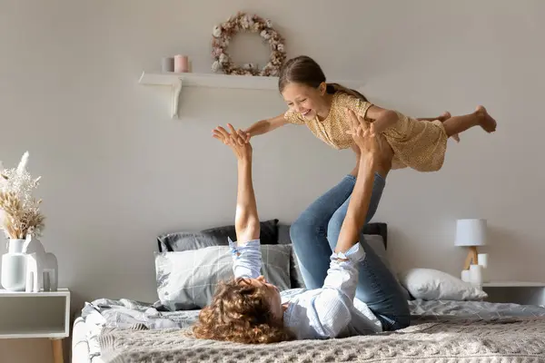 Energetic young mom lift little daughter in air on bed — Stock Photo, Image