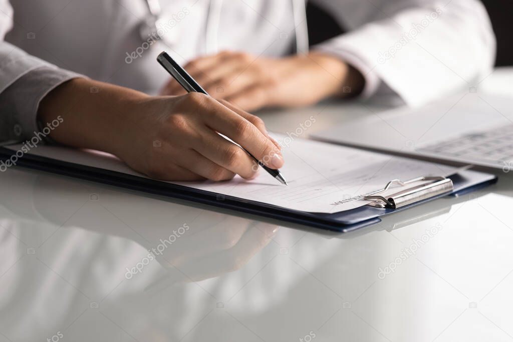 Close up professional female doctor taking notes, filling medical documents