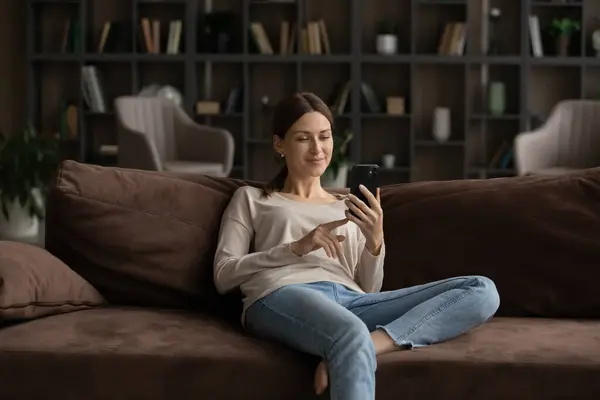 Kafkasyalı kadın kanepeye uzanıp akıllı telefon kullanıyor. — Stok fotoğraf