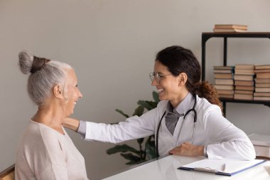 Gülümseyen doktor olgun hastanın omzuna dokunuyor. Haberler iyi.