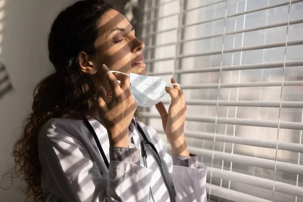 Close up tired female doctor taking off medical face mask — Stock Photo, Image