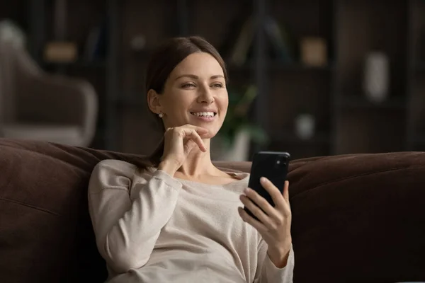 Smiling woman relax on sofa browsing web on cell