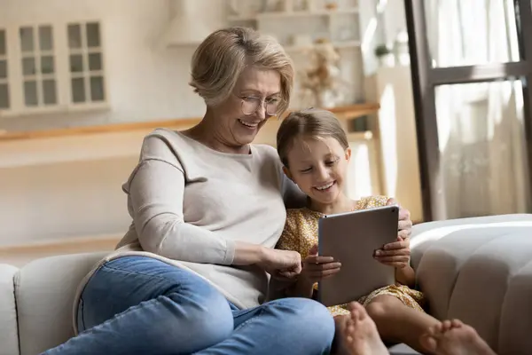 Sorrindo aposentado babá e menina assistir desenhos animados usando tablet — Fotografia de Stock