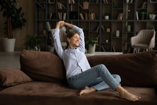 Happy young woman relax on couch at home stretching — Stock Photo, Image