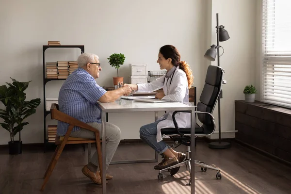 Gülümseyen kadın doktor ve olgun hasta el sıkışıyor.