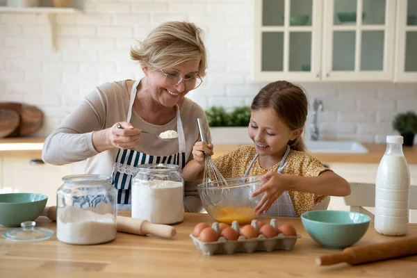 Menina feliz ajudar avó sênior na cozinha mistura massa — Fotografia de Stock