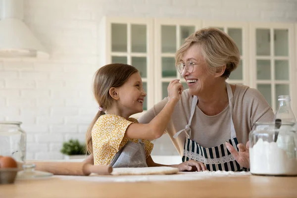 Laughing elderly granny and small grandchild painting noses with flour — Stock Photo, Image
