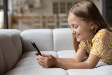 Kanepede uzanmış gülümseyen küçük çocuk telefon ekranına bak.