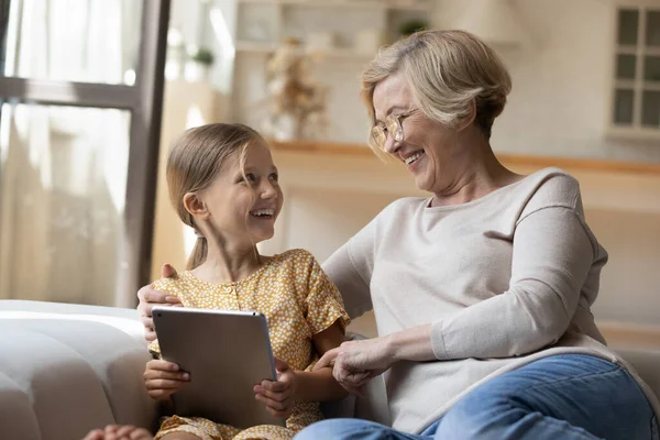 Laughing grandma hug small granddaughter discuss funny photo on pad — Stock Photo, Image