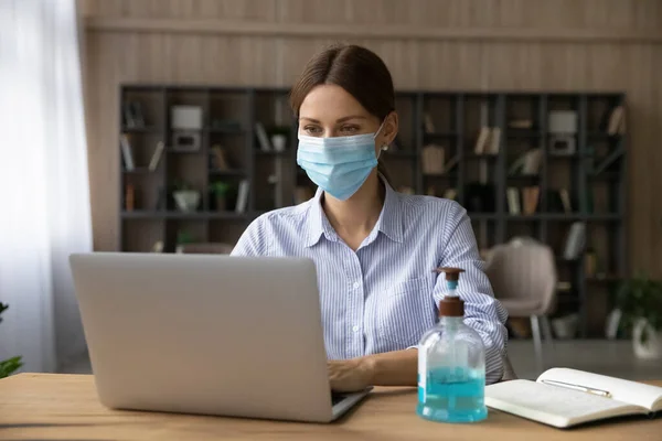 Kaukasiska kvinna i facemask arbete på laptop på nätet — Stockfoto