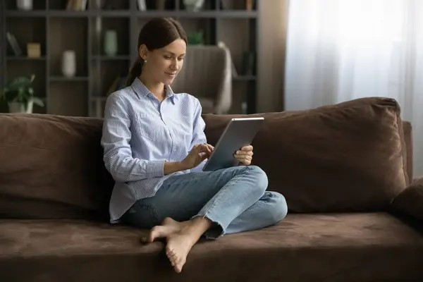 Mutlu kadın kanepeye uzanıp modern tablet kullanıyor. — Stok fotoğraf