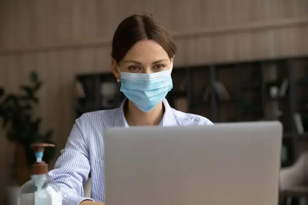 Affärskvinna i facemask arbete på laptop på nätet — Stockfoto