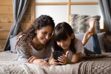 Mutlu anne ve küçük kızı akıllı telefondan internette geziniyor.