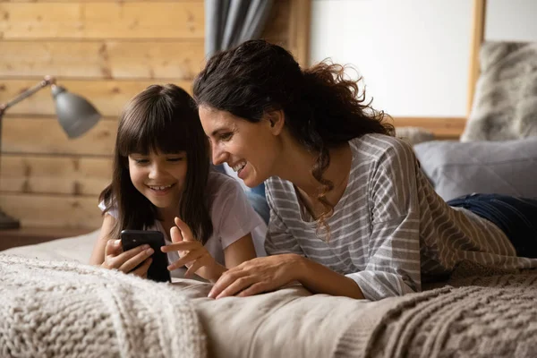 Посміхаючись, мама з донькою використовують мобільний. — стокове фото