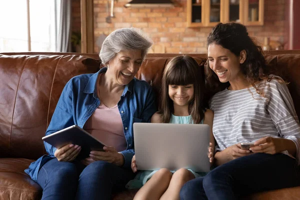 Feliz tres generaciones de mujeres relajarse en el sofá con gadgets — Foto de Stock