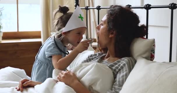 Grappig kind meisje doen alsof arts check moeder keel in slaapkamer — Stockvideo