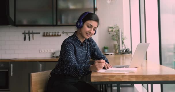 Jovem mulher de etnia indiana feliz em fone de ouvido sem fio estudando online. — Vídeo de Stock