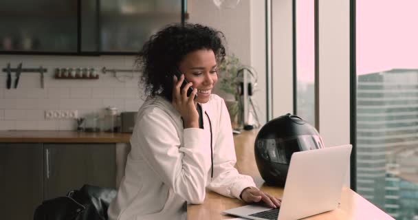 Feliz mujer de negocios africana sosteniendo la llamada móvil mientras trabaja en la computadora. — Vídeos de Stock