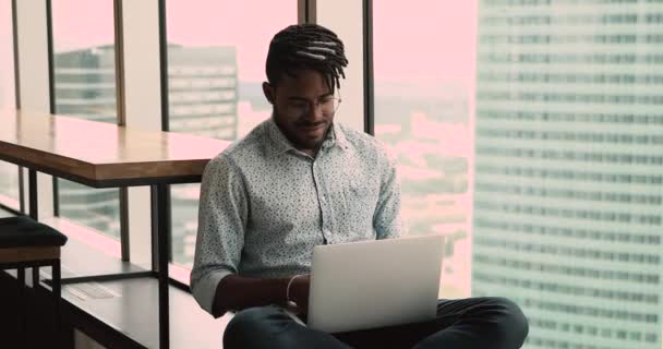 Šťastný mladý africký Američan pracující na počítači, sedí na parapetu. — Stock video