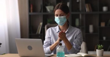 Maskeli genç iş kadını antibakteriyel jel ile ellerini dezenfekte ediyor..
