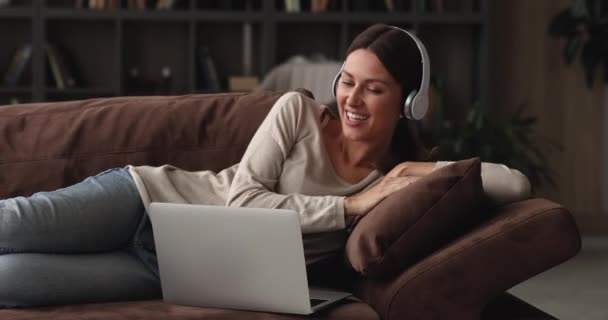 Щаслива молода жінка в бездротових навушниках тримає відеодзвінок з друзями . — стокове відео