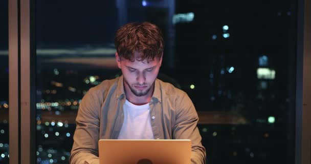 Koncentrerad ung 25-årig manlig frilansare som arbetar till sent på datorn. — Stockvideo