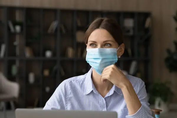 Trabajadora pensativa en máscara facial en el lugar de trabajo — Foto de Stock